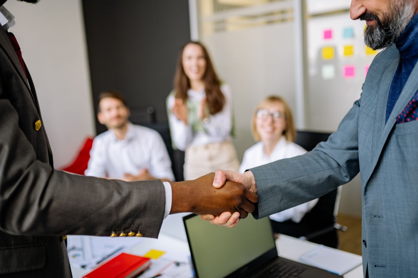 Two people shaking hands across a meeting table.