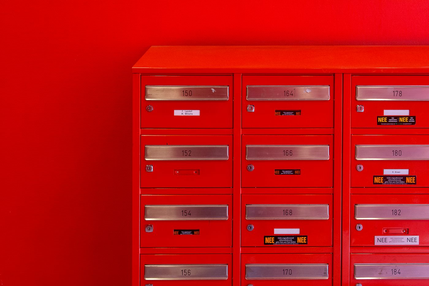 A wall of numbered red letterboxes, several carrying stickers refusing unaddressed advertising.