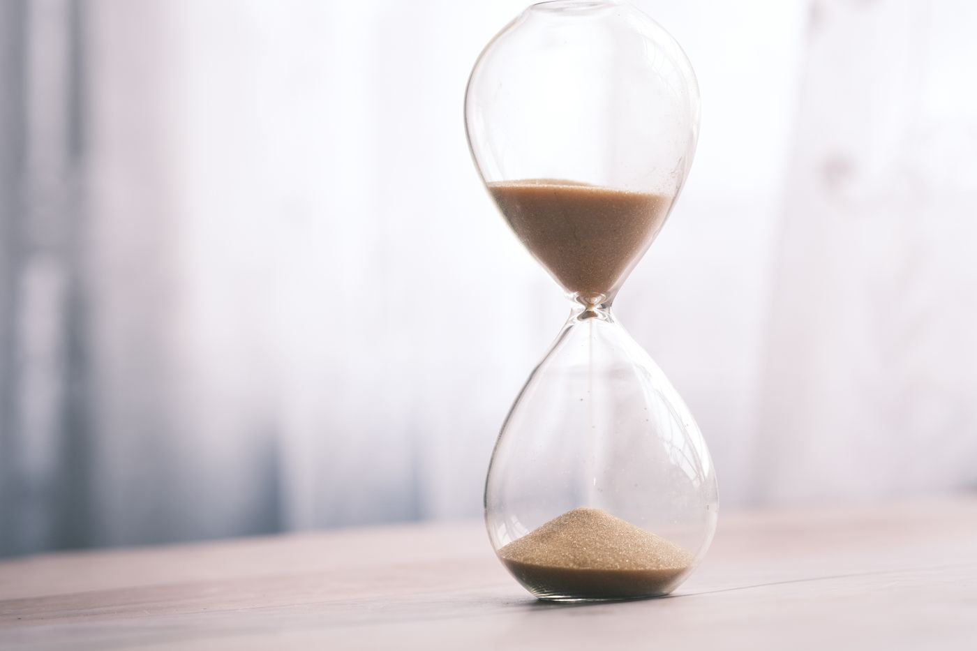 An hourglass with sand running through it on a wooden surface.
