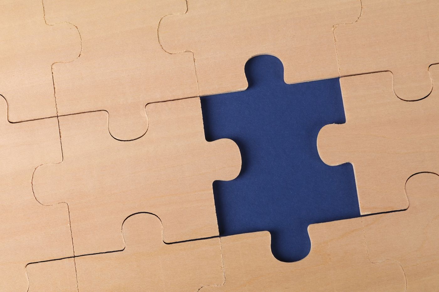 A wooden jigsaw puzzle with one piece missing, the blue board showing through the gap.