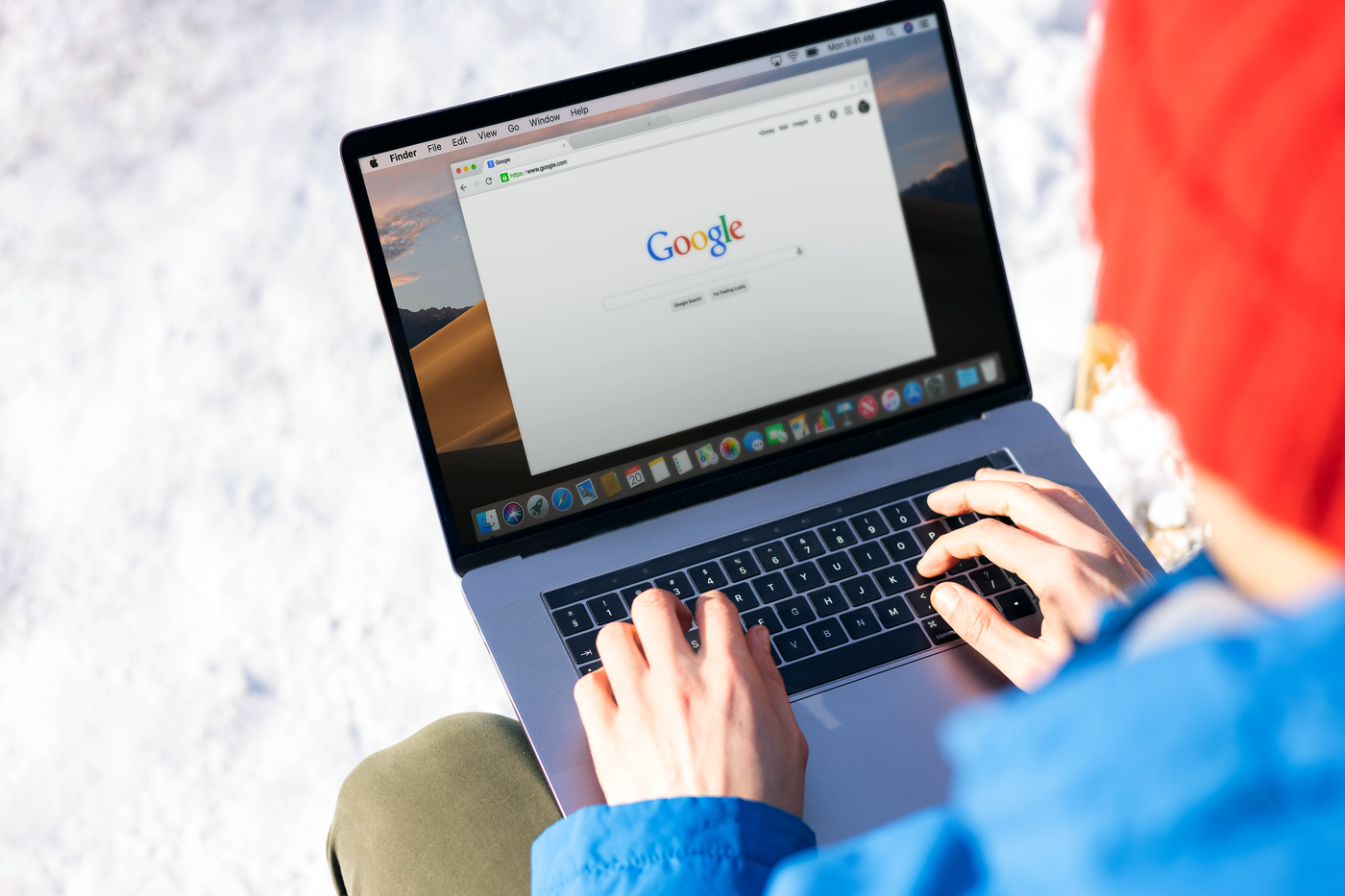 A person in a red hat typing on a laptop that shows the Google search page.