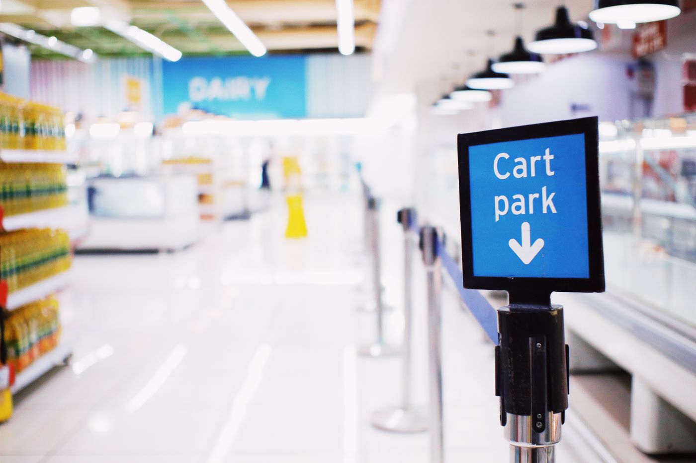 A sign on a post inside a bright supermarket, with the dairy aisle out of focus behind it.